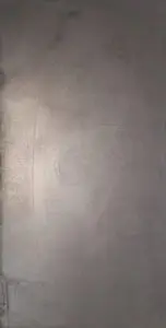 Eine stilvolle Wand im Wohnzimmer zeigt eine glatte, metallische Textur von ATHOS-Stahl, ideal für kreative Wandgestaltung.