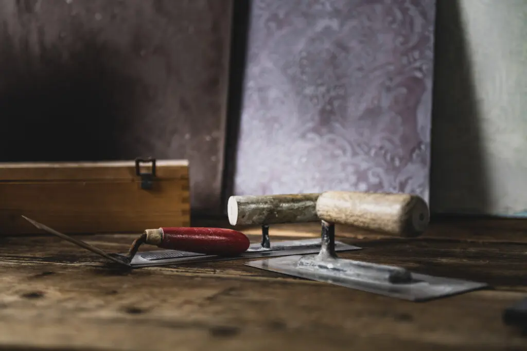 Auf einem Holztisch liegen Spachtelwerkzeuge vor kunstvoll gestalteten Wänden, perfekt für kreative Wandgestaltung mit Einhornwerke.