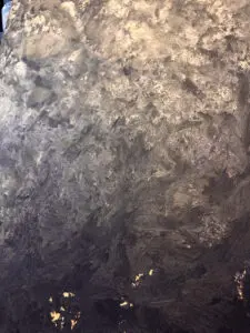 Die Wand zeigt eine MONROE-Effeckt-Wandbeschichtung mit metallischem Glanz, ideal für kreative Wohnzimmergestaltung.