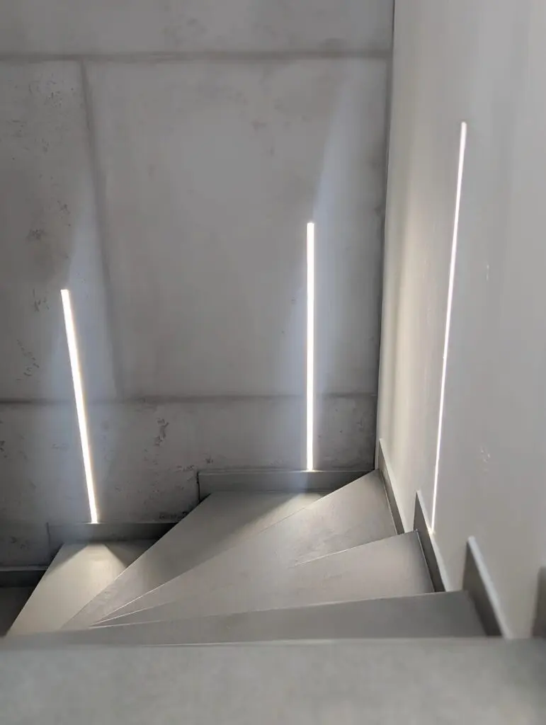 Eine fugenlos gespachtelte Treppe in Betonoptik erzeugt eine moderne Wandgestaltung im hellen Treppenhaus.