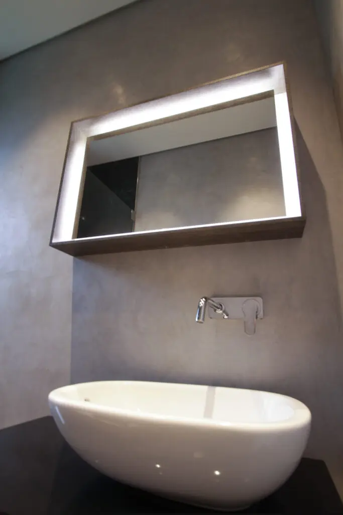 Badezimmer mit grauer STUCCORINO Lustro Wand, Aufsatzwaschbecken und beleuchtetem Spiegelkasten