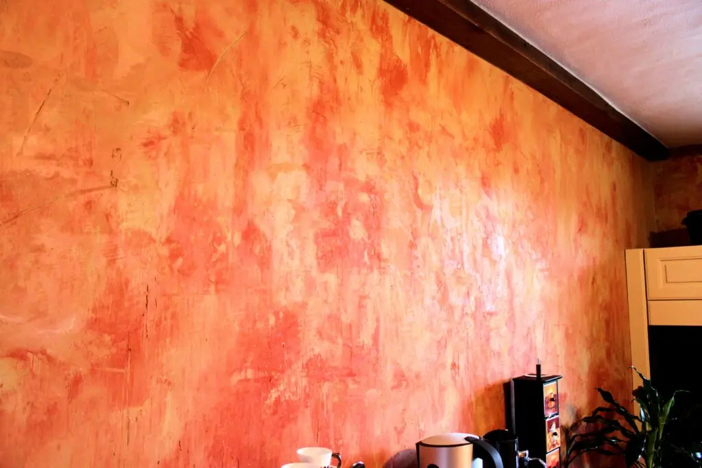 Eine orangefarbene Wohnzimmerwand ist mit dem schimmernden Streichputz Oberflaeche-STUCCORINO Trash kreativ gestaltet.