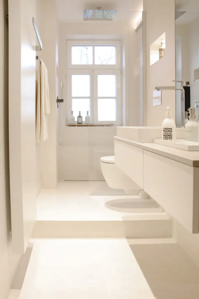 Schmales weißes fugenloses Bad mit Stufe, Regendusche am Fenster und wandhängendem WC