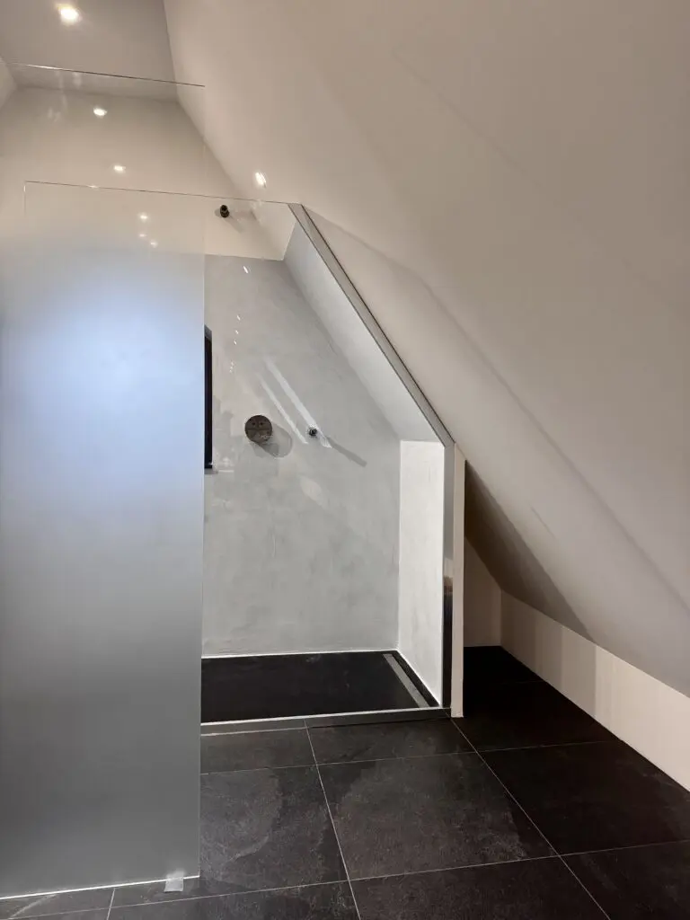 Dusche unter Dachschräge mit fugenloser hellgrauer Wandfläche, Milchglas und dunklem Fliesenboden