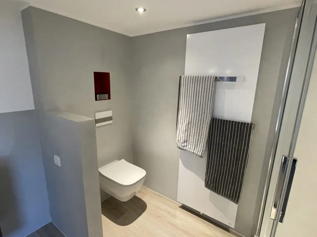 Ein modernes Badezimmer zeigt eine stilvolle Wandgestaltung in sanften Grautönen mit Handtüchern und diskretem Streichputz.