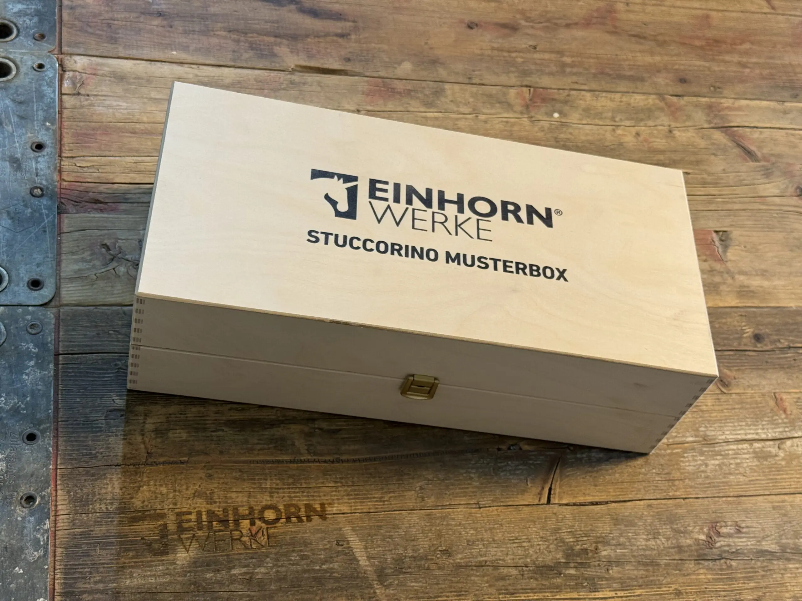 Die STUCCORINO-Musterbox von Einhornwerke liegt auf einem rustikalen Holztisch und inspiriert zur kreativen Wandgestaltung.