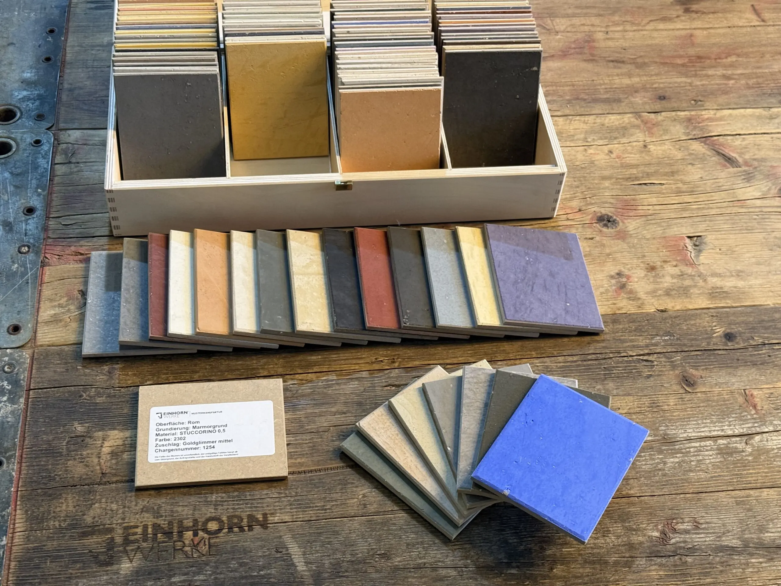 Eine STUCCORINO-Musterbox von Einhornwerke zeigt verschiedene Farbmuster für kreative Wandgestaltung auf einem Holztisch.