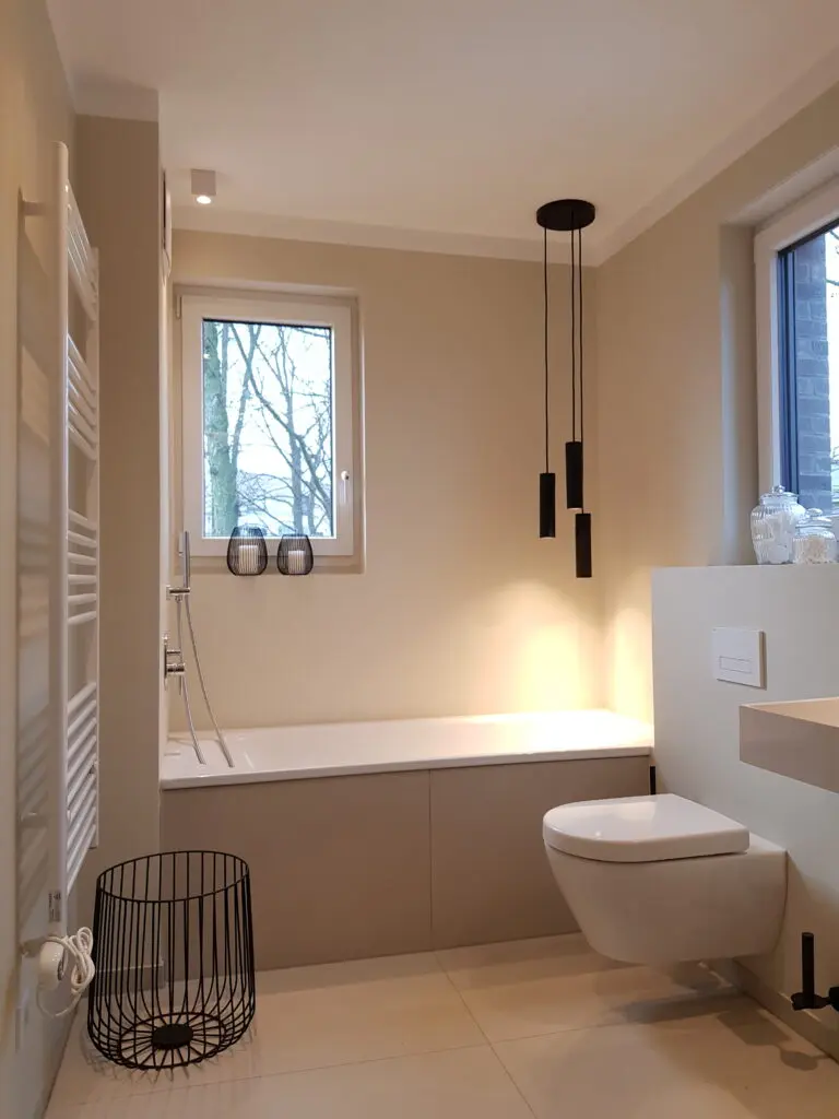 Bad mit beigen fugenlosen Wänden, Badewanne unter Fenster und schwarzer Pendelleuchte