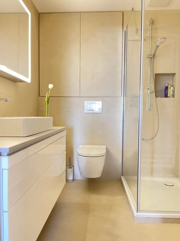 Bad in Beige mit fugenlosen Wandflächen, Hänge-WC, Duschkabine mit Nische und weißem Waschtisch