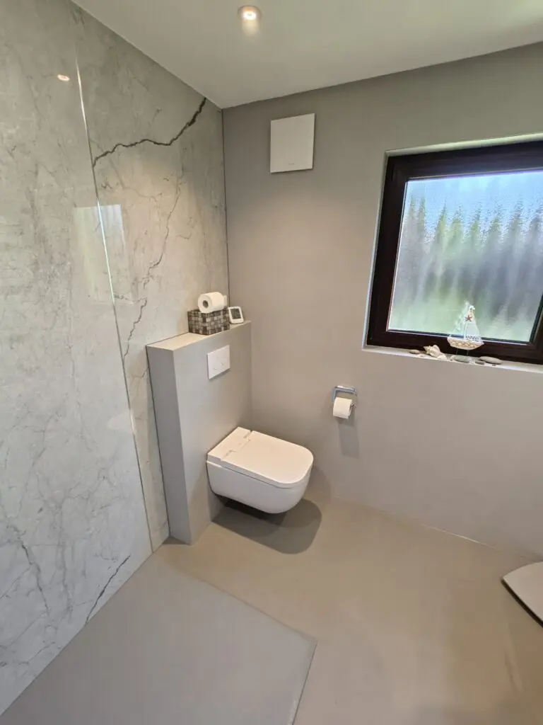 Bad mit Dusche vor Wand in Marmoroptik, Hänge-WC und hellgrauem fugenlosem Boden