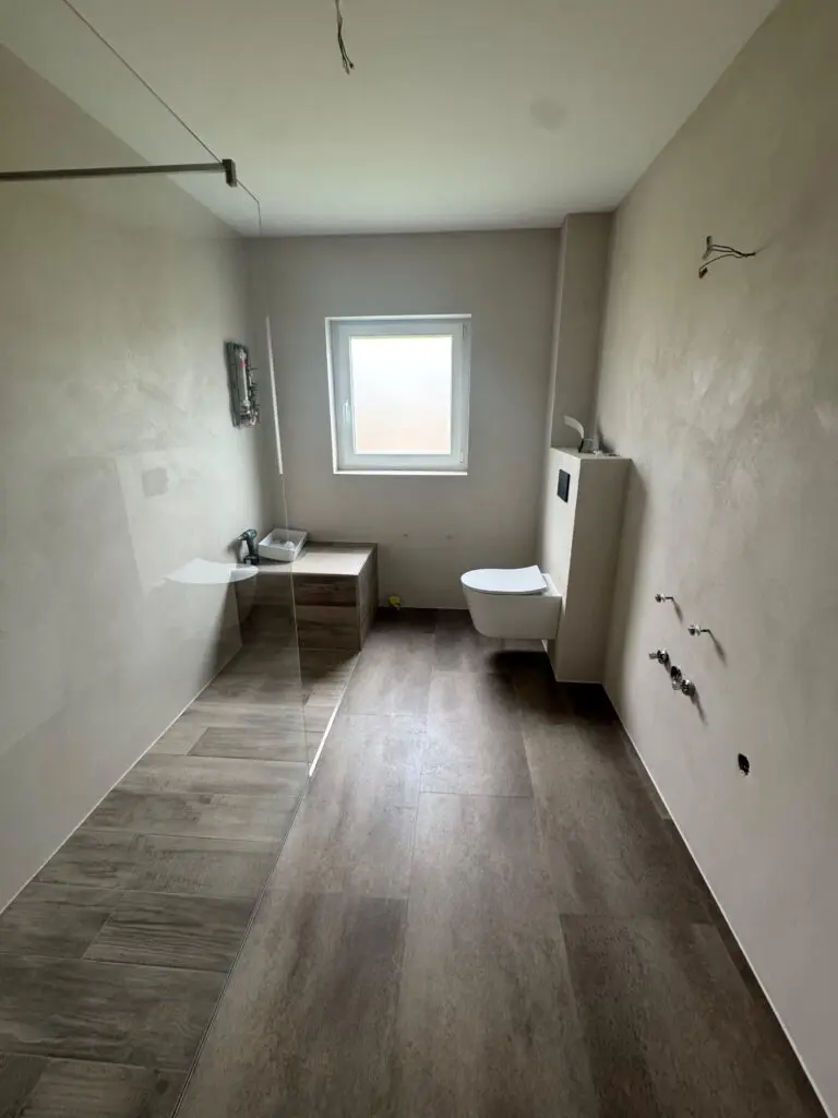 Unmöbliertes Bad mit bodengleicher Dusche, Spachtelboden in Dielenoptik und hellen fugenlosen Wänden