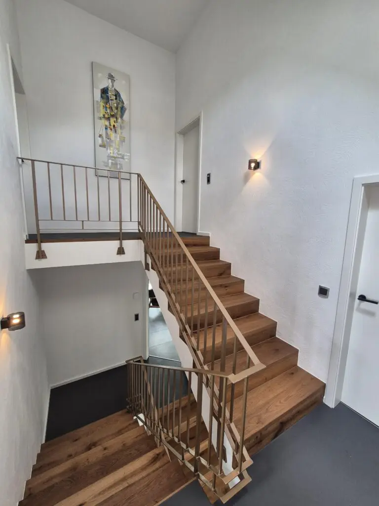 Treppenhaus mit Holzstufen und Metallgeländer, hellen Wänden und grauem Spachtelboden auf den Podesten