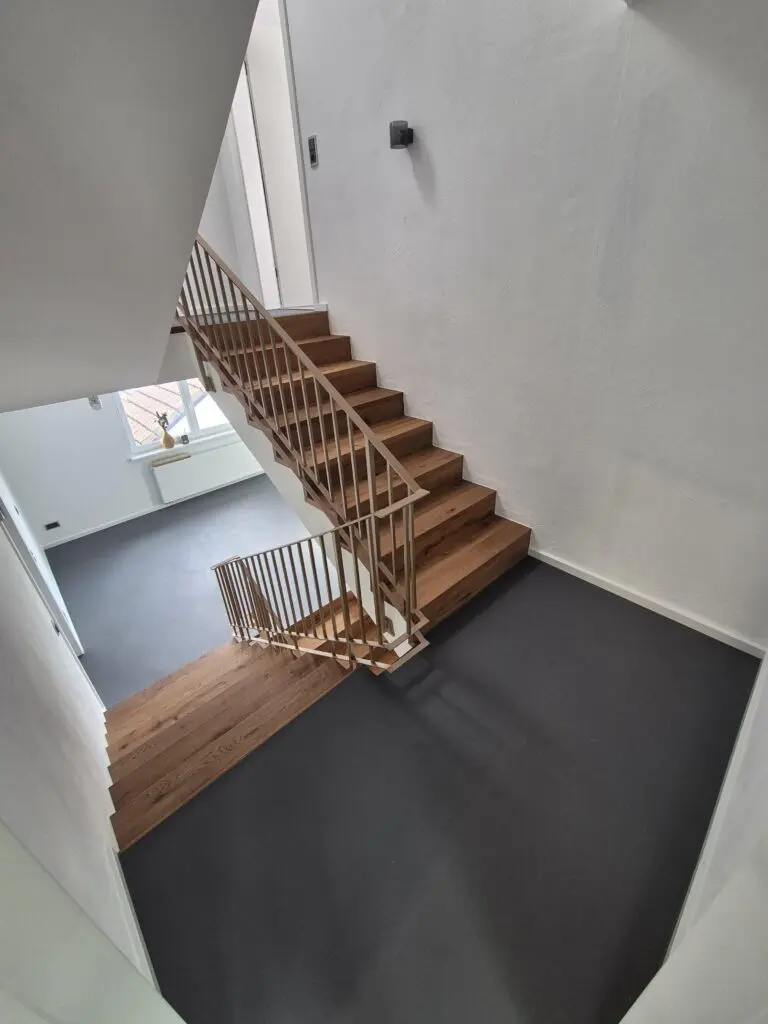 Blick von oben in ein Treppenhaus mit Eichenstufen und anthrazitfarbenem Spachtelboden