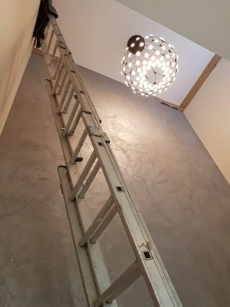 Eine Leiter steht in einem Treppenhaus mit kreativer Wandgestaltung und einer modernen Deckenlampe.