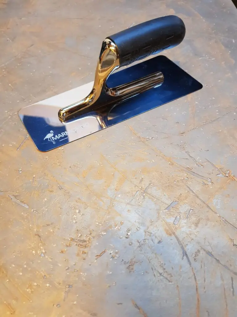 Ein glänzender Glättspachtel liegt auf einer strukturierten Oberfläche, ideal für kreative Wandgestaltung im Wohnzimmer.