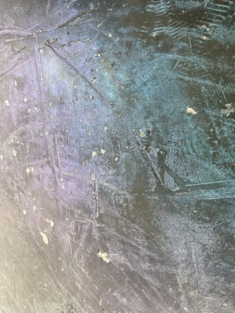 Die moderne Wandgestaltung im Wohnzimmer zeigt eine schimmernde Oberfläche mit Textur in Blau- und Lilatönen.