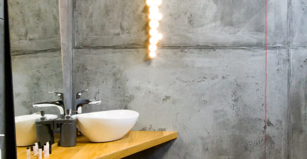 Ein modernes Badezimmer zeigt eine stilvolle rustikale Betonoptik mit einem eleganten Waschbecken auf einem Holztresen.