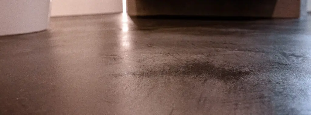 Bodennahe Aufnahme eines dunklen Sichtbetonbodens mit Kellenspuren neben freistehender Wanne