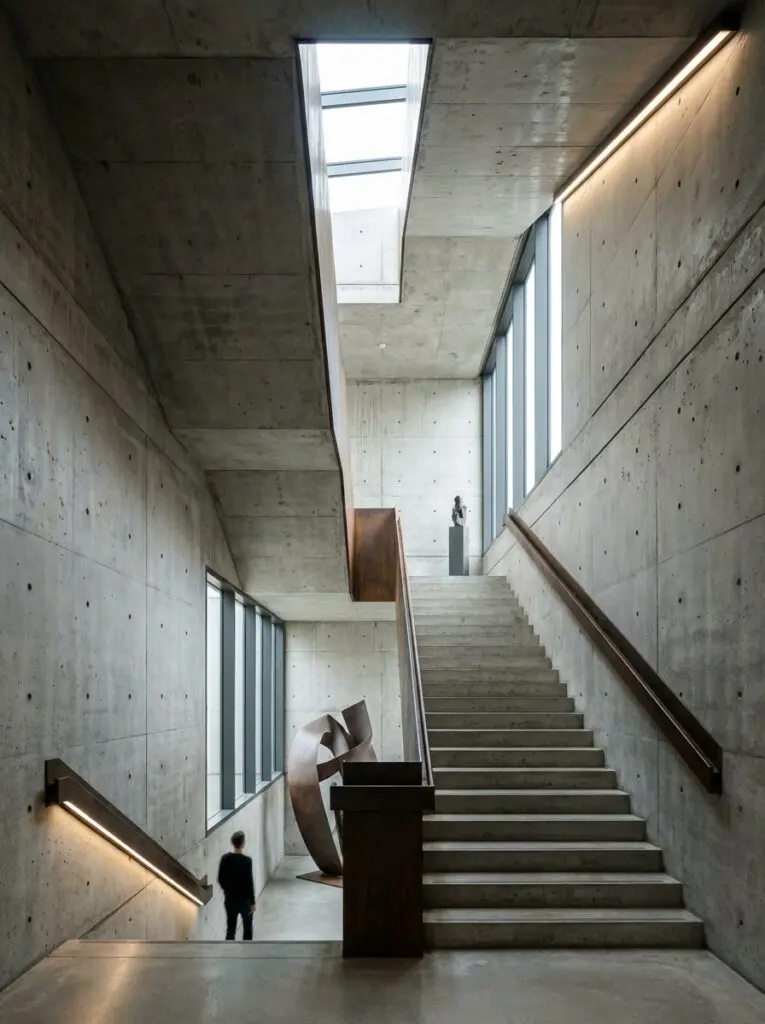 Ein modernes Treppenhaus in Betonoptik mit kreativer Wandgestaltung und Skulptur von Einhornwerke zieht die Blicke auf sich.