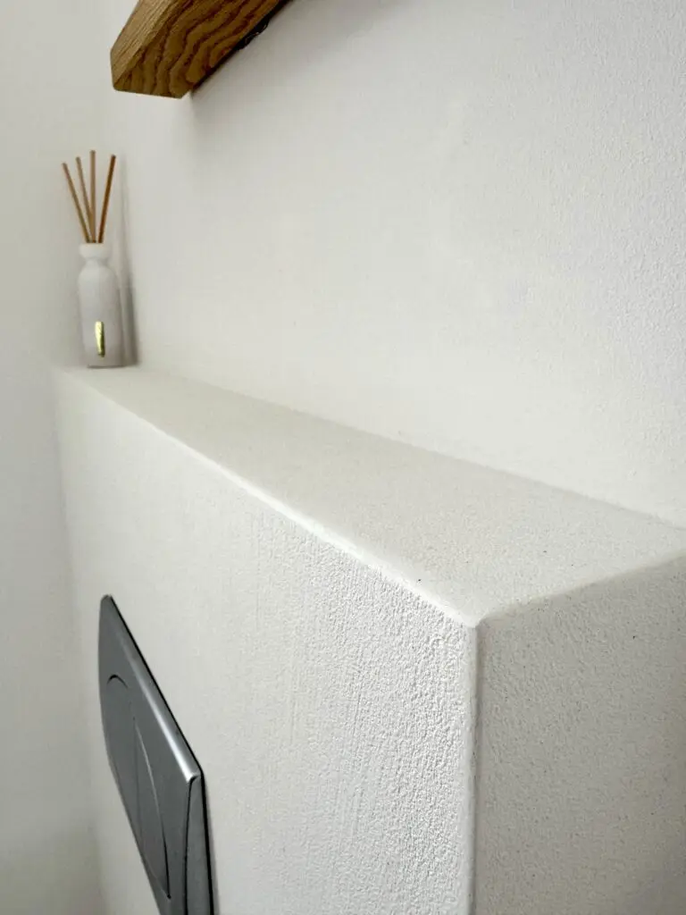 Nahaufnahme weiße Vorwandverkleidung mit feinkörnigem Strukturputz und WC-Drückerplatte