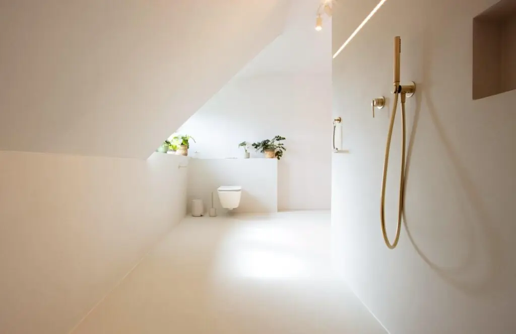Dachbad mit weißen fugenlosen Wänden und Boden, bodengleicher Dusche und goldfarbener Armatur