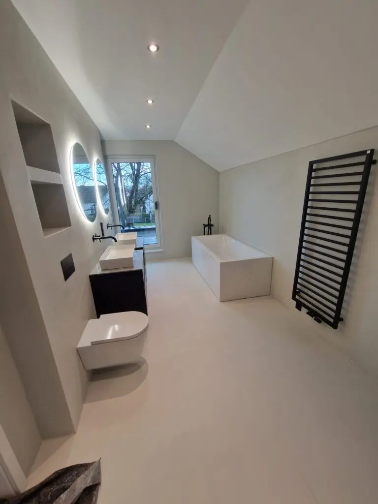 Dachgeschossbad mit hellem fugenlosem Boden und Wänden, Badewanne und schwarzem Handtuchheizkörper