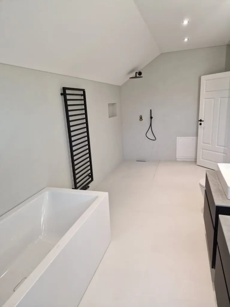 Helles fugenloses Bad mit bodengleicher Dusche, rechteckiger Badewanne und Weißlack-Tür