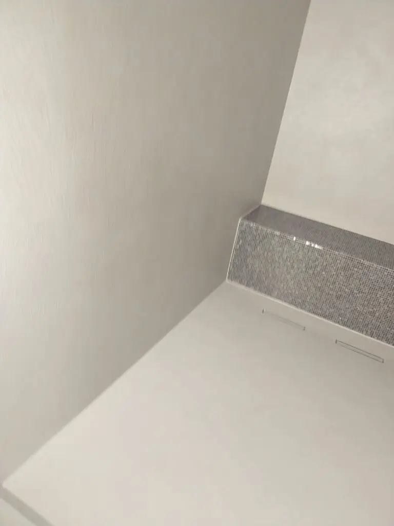Duschecke mit hellgrauem fugenlosem Boden und Wänden neben grauer Mosaik-Sitzbank