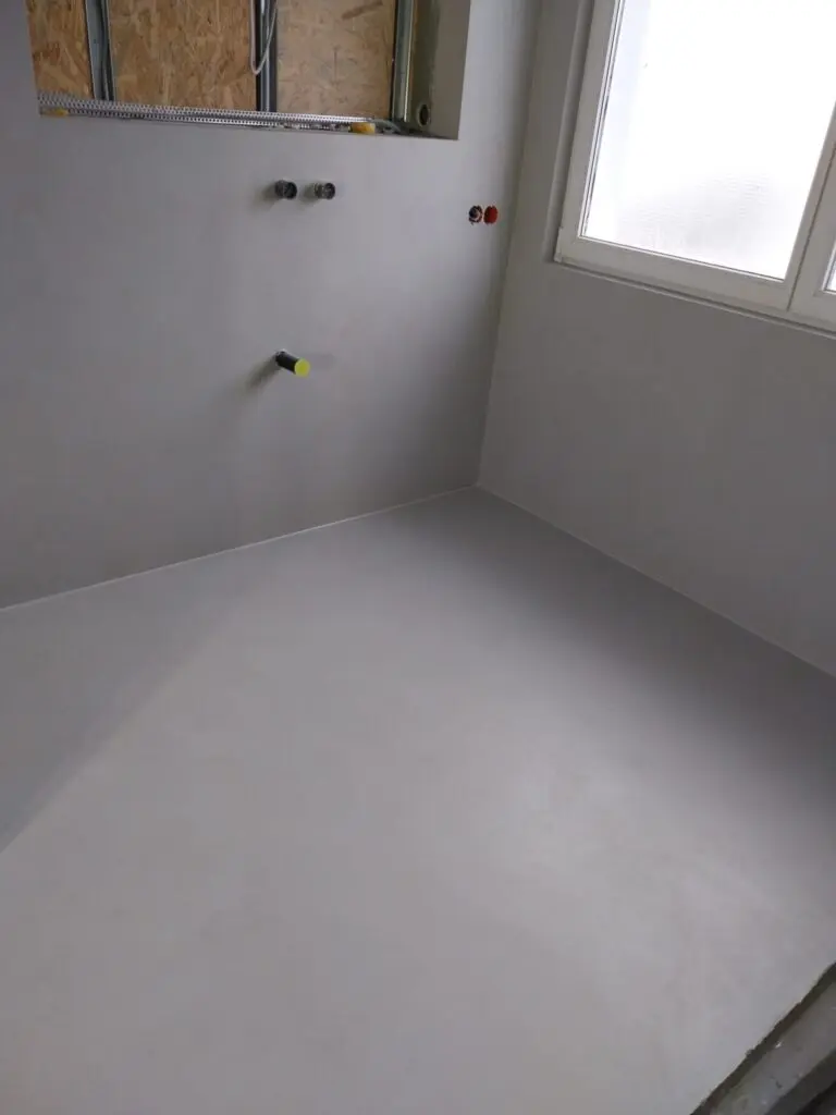 Bad im Rohbau mit hellgrau beschichteten fugenlosen Wänden und Boden vor der Installation