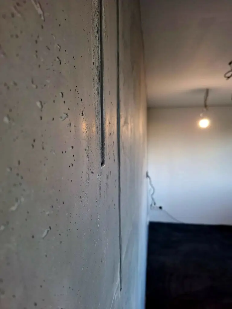 Wandfläche in Betonoptik mit Lunkern und Fugenlinien im Streiflicht eines unfertigen Raums
