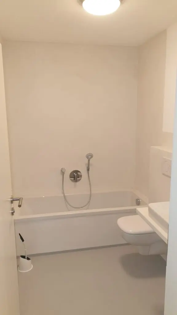 Kleines helles Bad mit fugenlosen Wandflächen um Badewanne, Wand-WC und grauem Boden