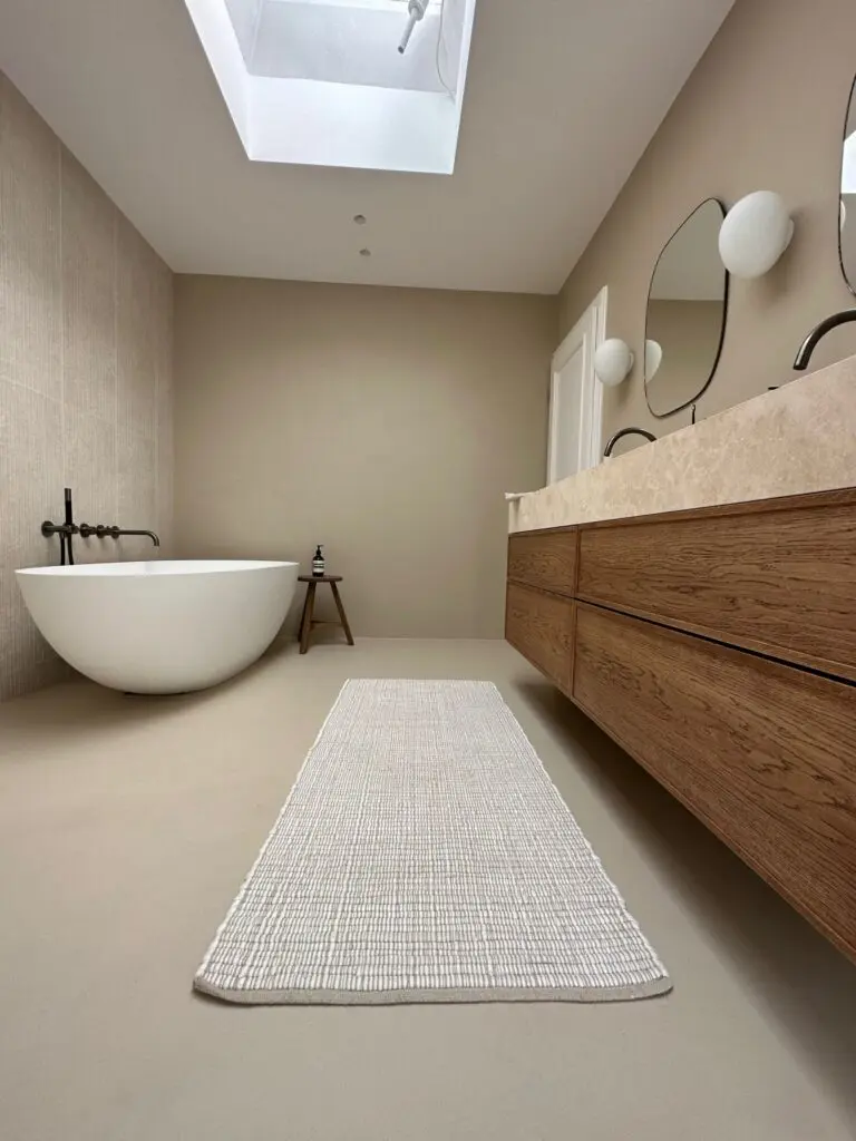 Bad mit beigen fugenlosen Wänden und Boden, freistehender Wanne, Holzwaschtisch und Dachfenster