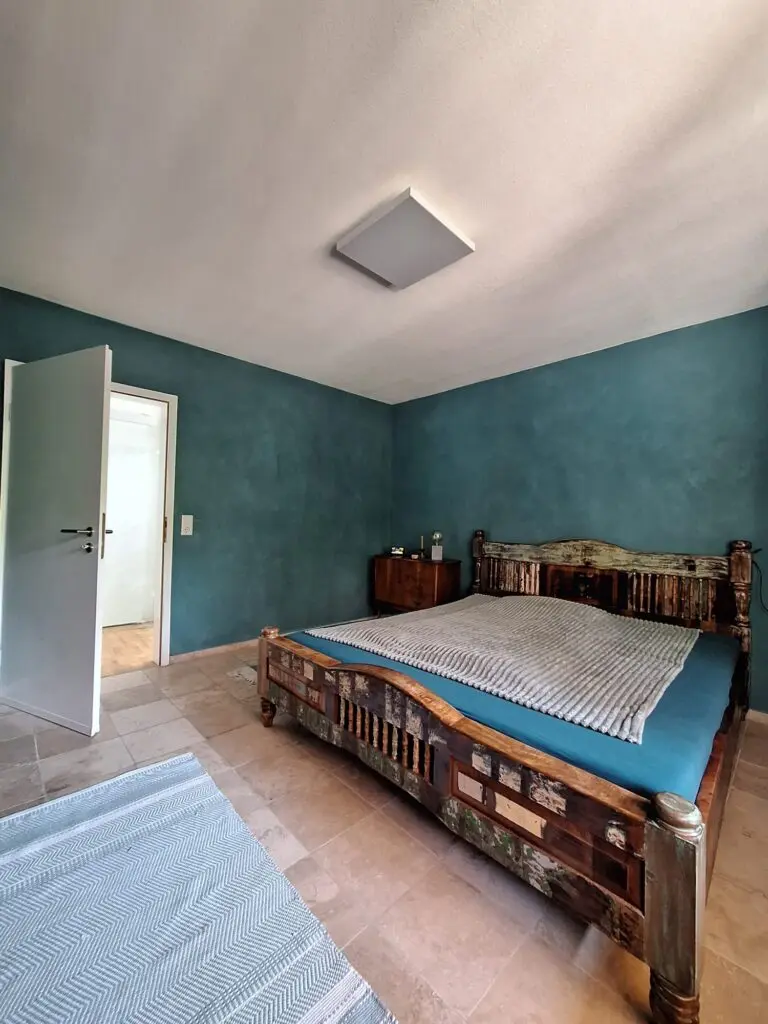 Schlafzimmer mit petrolblauen strukturierten Wänden, Holzbett und Natursteinboden
