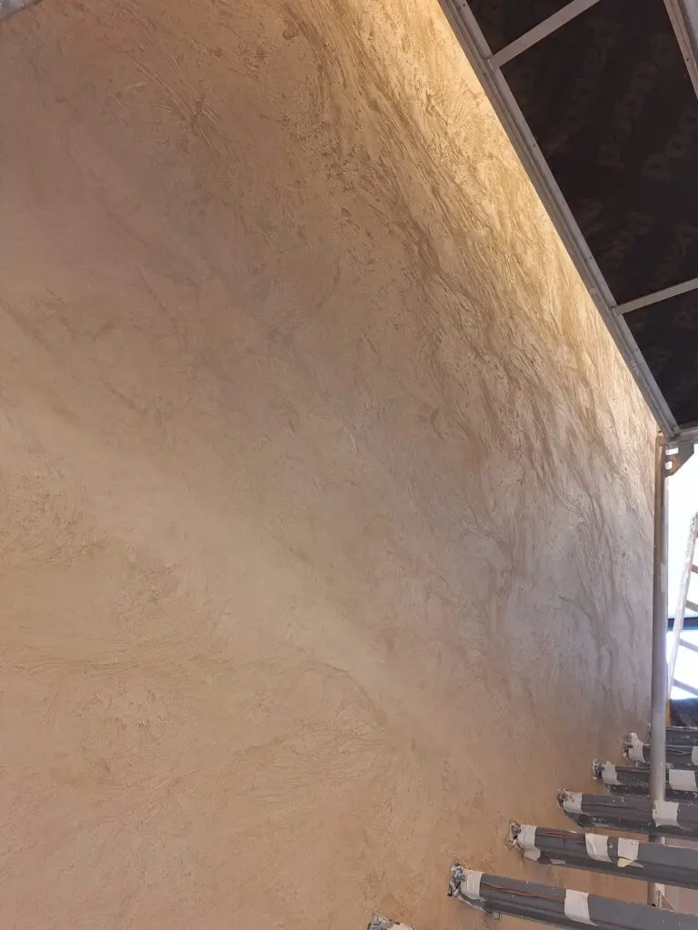 Sandfarbene Spachteltechnik mit bewegter Struktur auf großer Wand im Streiflicht unter Glasdach