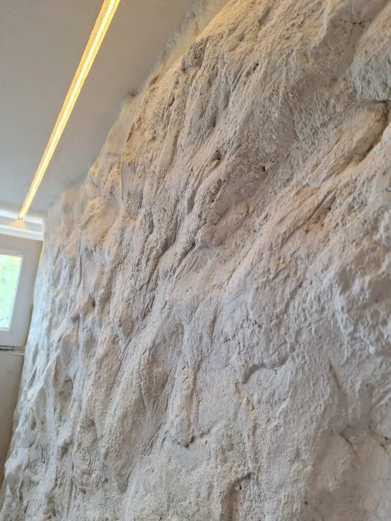 Weiße Wand mit grob modellierter Felsstruktur unter LED-Lichtleiste