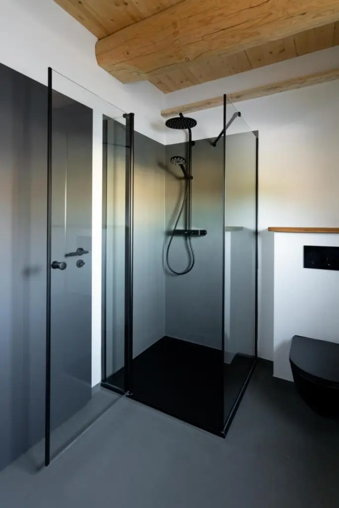 Begehbare Dusche mit Glaswand, dunkelgrauen fugenlosen Wänden und Boden unter Holzbalkendecke