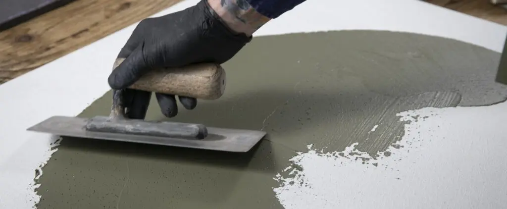 Ein Handwerker trägt STUCCORINO-Pigment mit einer Glättkelle auf eine vorbereitete Fläche für einen fugenlosen Boden auf.