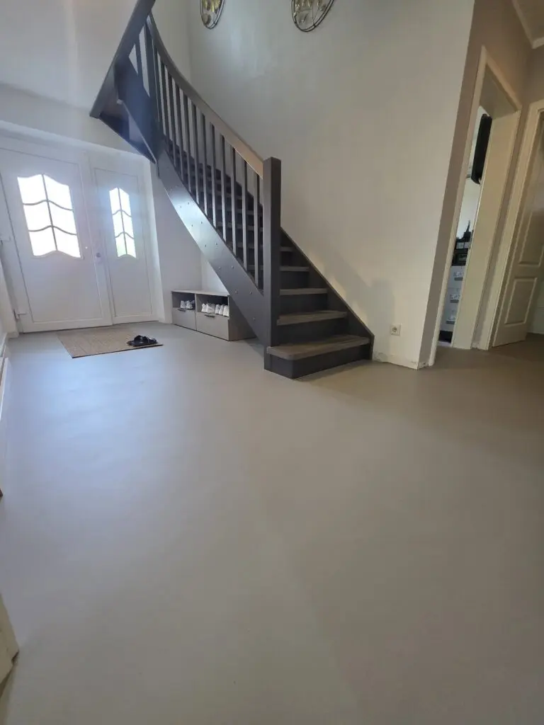 Eingangshalle mit großflächigem grauem Microzementboden, Haustür und dunkler Treppe