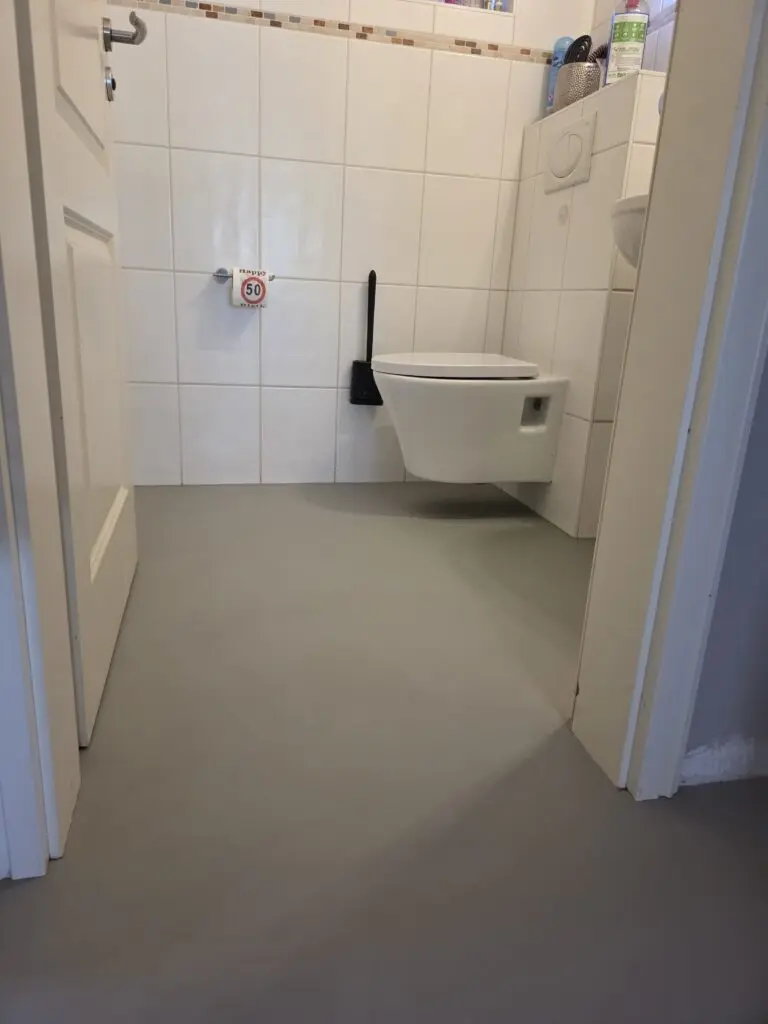 Gäste-WC mit grauem fugenlosem Microzementboden und weiß gefliesten Wänden