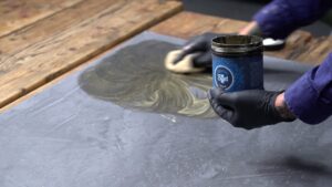 Ein Handwerker trägt den 2-STUCCORINO-Effect dünn auf die durchgetrocknete STUCCORINO-Oberfläche auf einem Tisch auf.