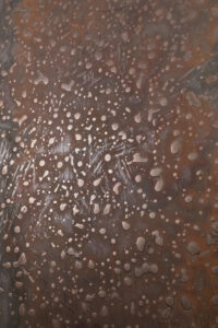 Eine Wand zeigt eine kreative Gestaltung mit Zinnbronze-Patina und flüssigem Metall, ideal für stilvolle Wohnzimmer.