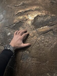 Eine Hand berührt eine kunstvoll strukturierte Wand mit edler Metalloptik, ideal für kreative Wandgestaltung im Wohnzimmer. Rezept: Unikat