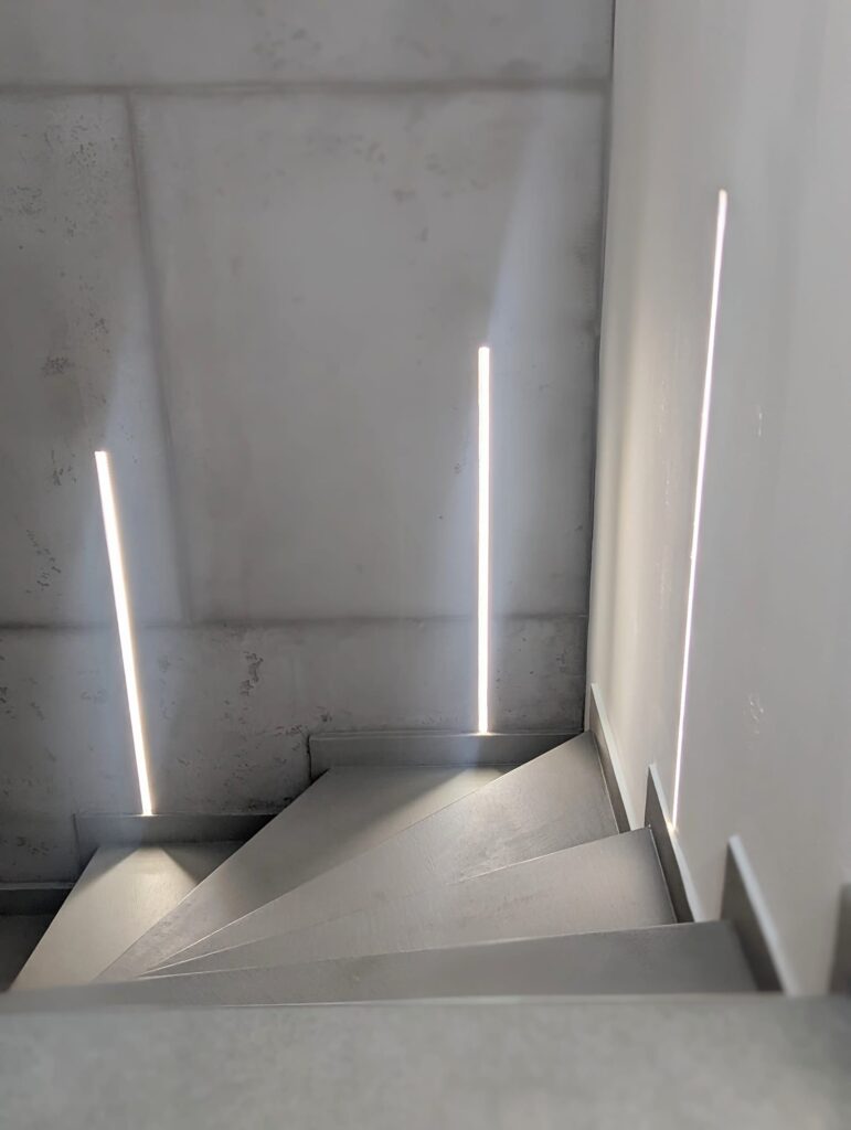 Eine fugenlos gespachtelte Treppe in Betonoptik erzeugt eine moderne Wandgestaltung im hellen Treppenhaus.