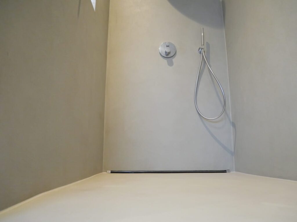 Ein modernes, fugenloses Badezimmer mit minimalistischer Wandgestaltung und einer eleganten Dusche ohne Fliesen.