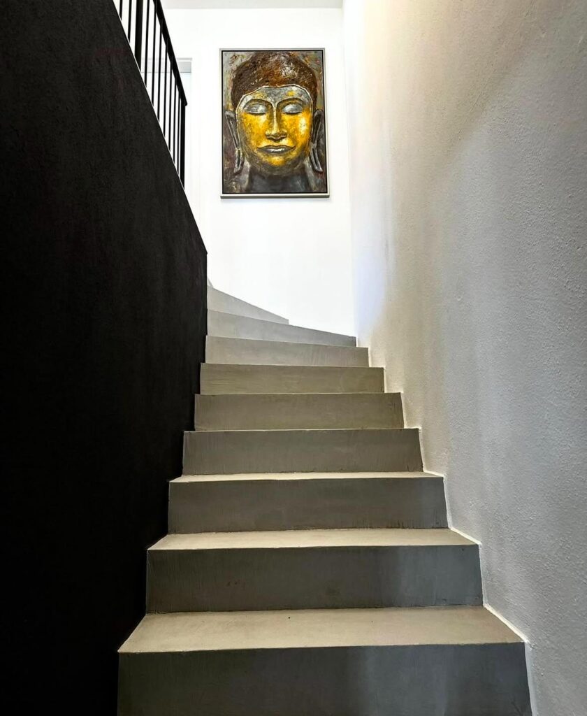 Eine fugenlose Betontreppe führt zu einem goldenen Buddha-Bild, eingerahmt von stilvoller Wandgestaltung.