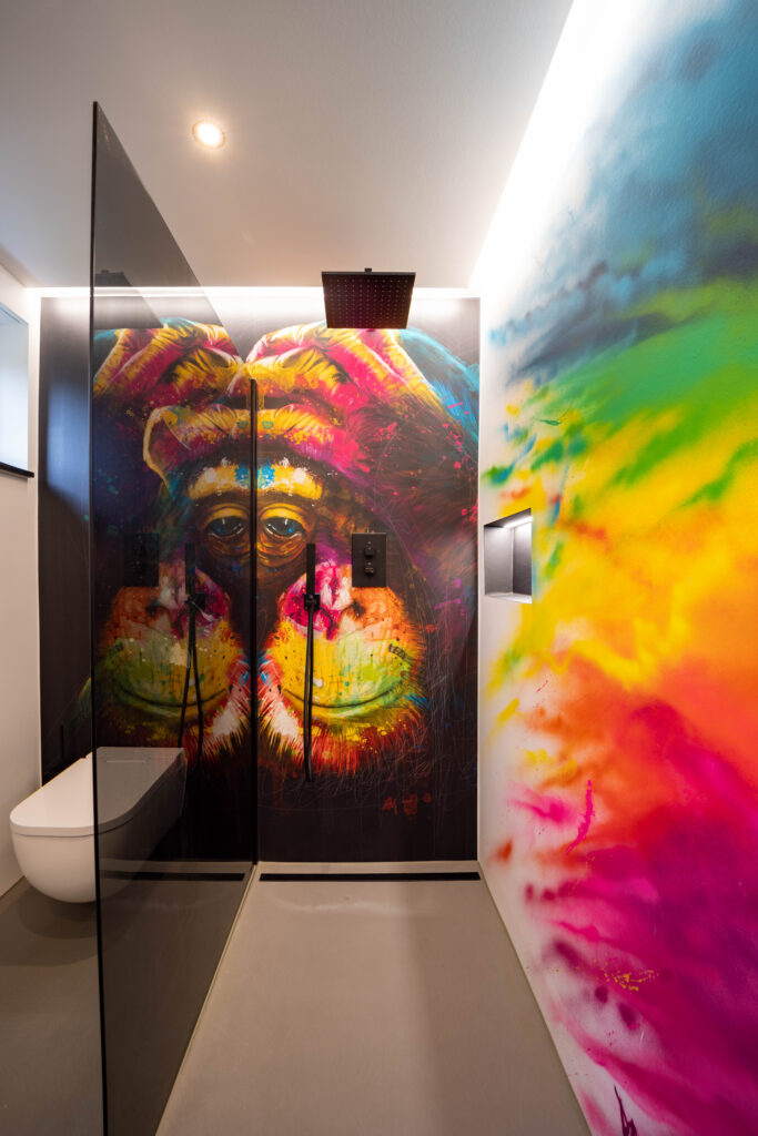 Ein modernes Badezimmer zeigt kreative Wandgestaltung mit buntem Kunstwerk und stilvollem Spachtelboden von Einhornwerke.