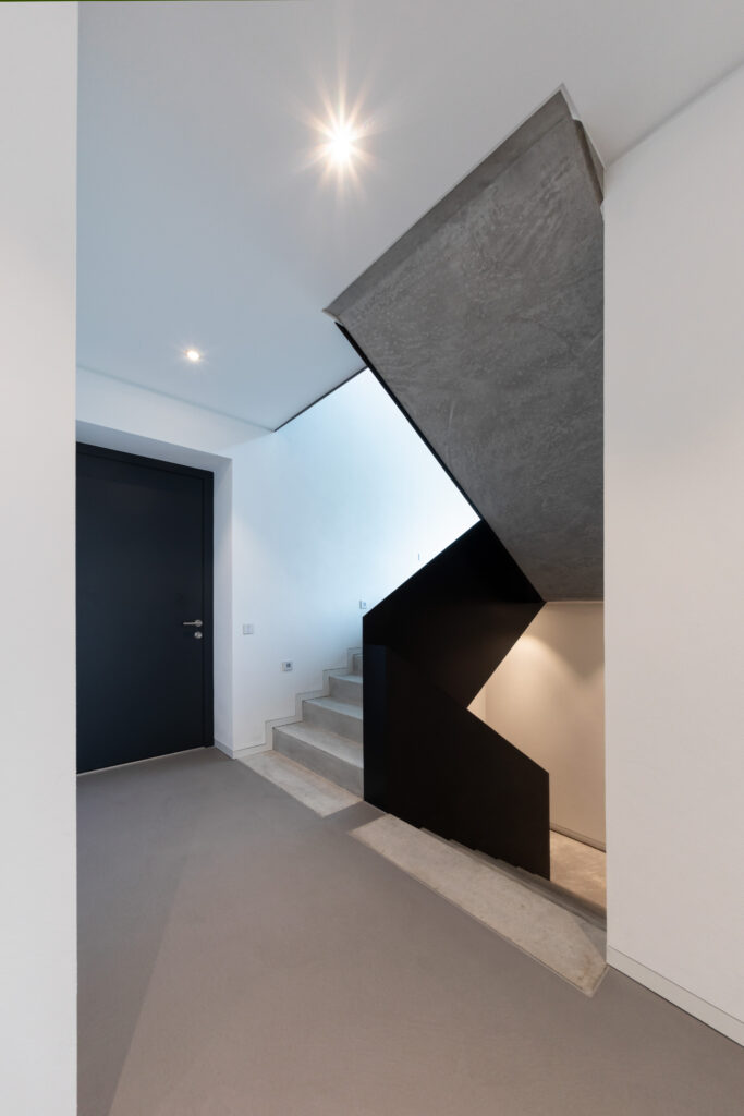 Eine moderne, minimalistische Treppe mit fugenlos gespachteltem Boden zeigt kreative Wandgestaltung im Eingangsbereich.