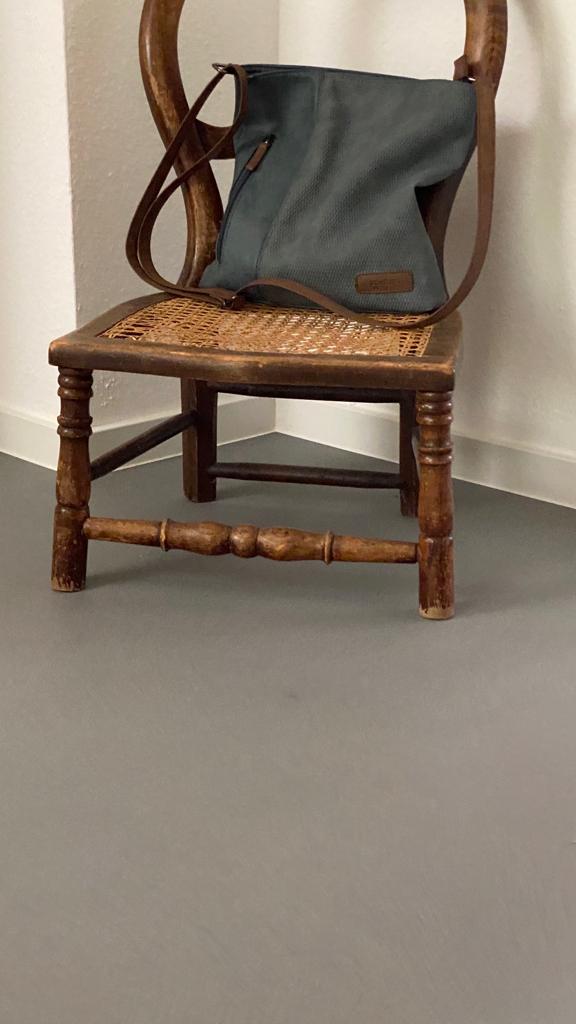 Ein rustikaler Holzstuhl mit einer Tasche steht auf einem eleganten, grauen Spachtelboden von Einhornwerke.