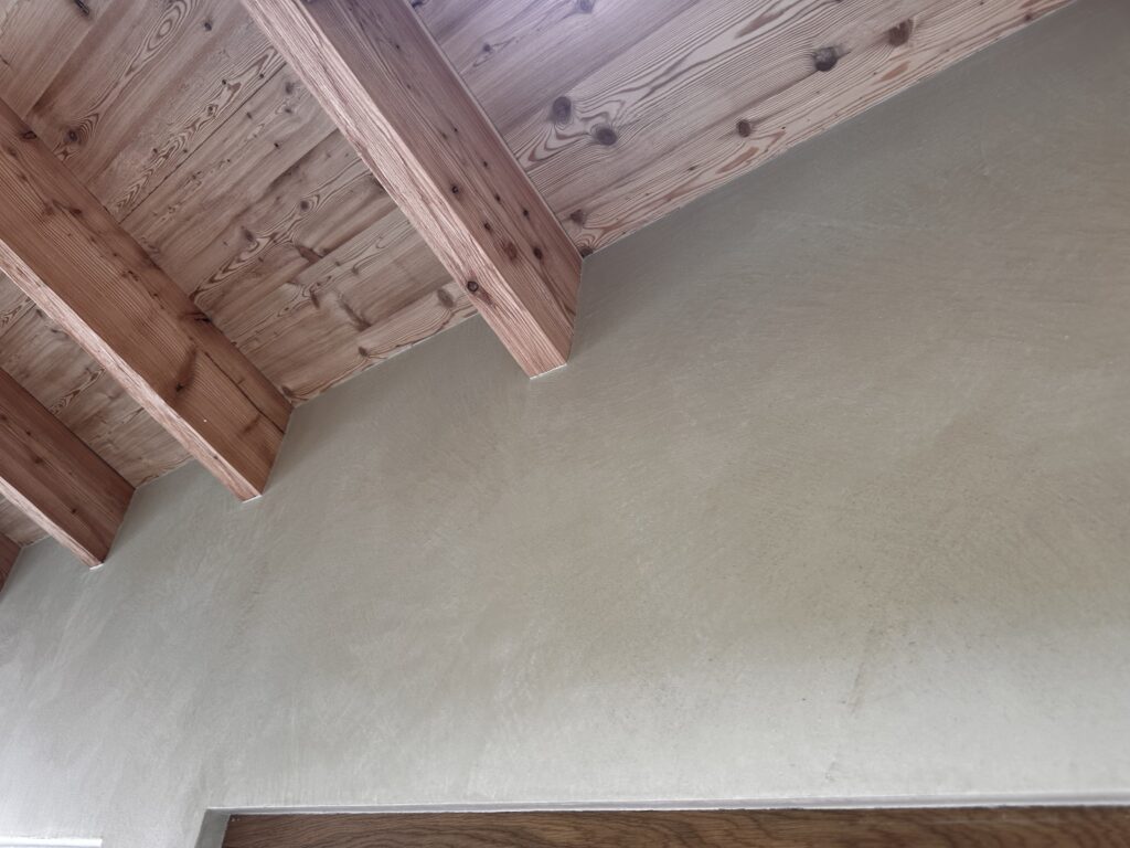 Eine stilvolle Wandgestaltung mit Marmorea Kalkputz ergänzt die natürliche Holzdecke im Wohnzimmer.