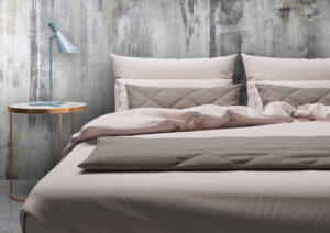 Ein stilvolles Schlafzimmer mit einer Wand aus STUCCORINO Fresco-Natur und einem eleganten Bett in sanften Tönen.